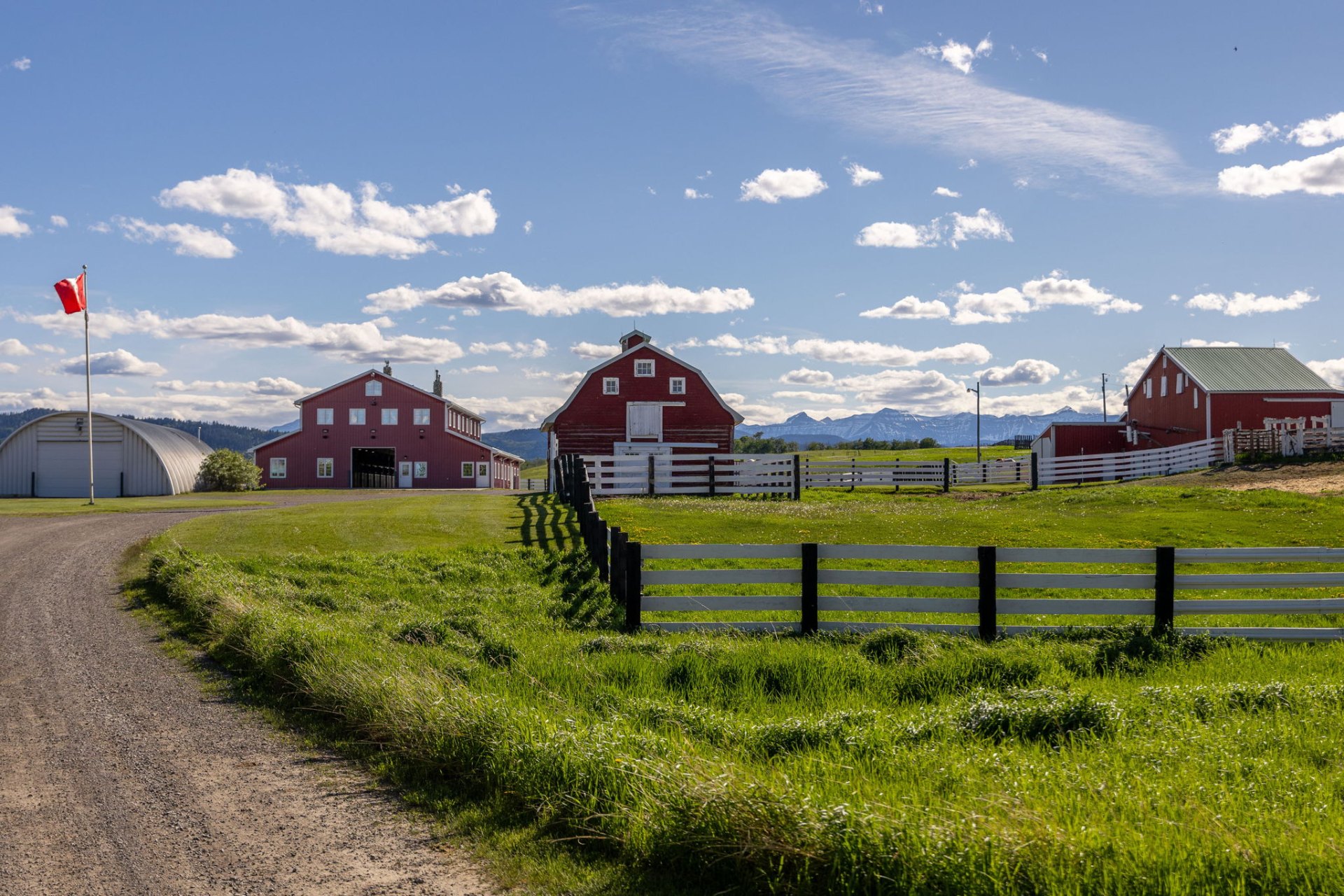 Ground-level view of the Quonset shop, the red barn residence, and the old barn with Rocky Mountains beyond